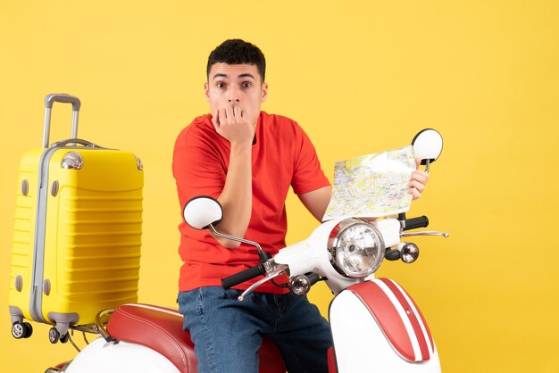 Vorderansicht verwirrter junger Mann in der Freizeitkleidung auf Moped, das Karte hält