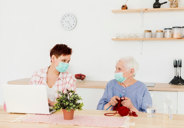 Vorderansicht von älteren Frauen, die zu Hause medizinische Masken tragen, während Aktivitäten ausgeführt werden