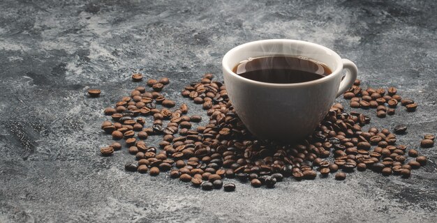 Vorderansicht von braunen Kaffeesamen mit Tasse Kaffee auf dunkler Oberfläche