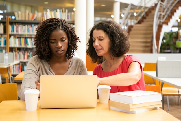 Vorderansicht von den ernsten Frauen, die bei Tisch sitzen und Laptop verwenden