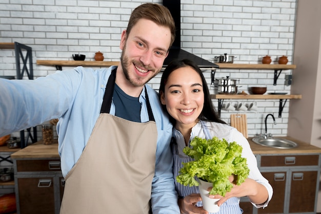 Vorderansicht von den Paaren, die selfie mit der Frau halten frischen grünen Kopfsalat in der Küche gefangennehmen