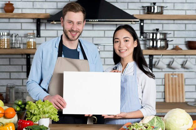 Vorderansicht von den schönen Paaren, die weißes leeres Papier in der Küche zeigen