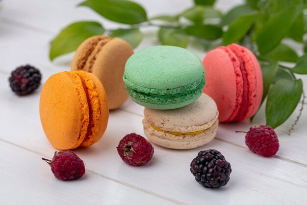 Vorderansicht von farbigen Macarons mit Brombeeren und Himbeeren auf einer weißen Oberfläche