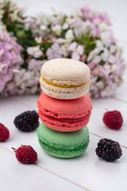 Vorderansicht von farbigen Macarons mit Brombeeren und Himbeeren auf einer weißen Oberfläche