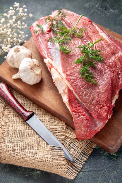 Vorderansicht von frischem rohem rotem Fleisch, grünem Knoblauch, Zitronensalz auf braunem Holzschneidebrettmesser auf nacktem Farbtuch auf dunklem Hintergrund