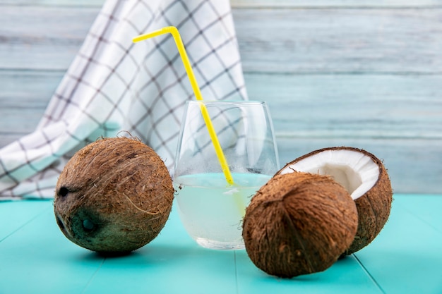 Vorderansicht von frischen Kokosnüssen mit einem Glas Wasser auf Tischdecke und grauer Holzoberfläche