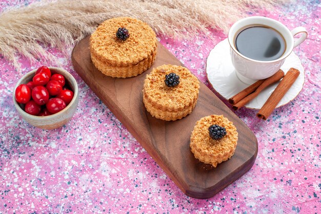 Vorderansicht von kleinen köstlichen Kuchen rund gebildet mit Zimt und Tee auf der rosa Oberfläche