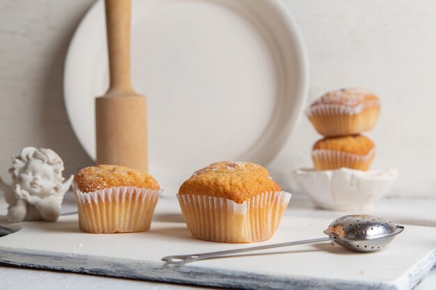 Vorderansicht von kleinen Kuchen innerhalb der Papierformen mit Zuckerpulver auf dem weißen Schreibtisch