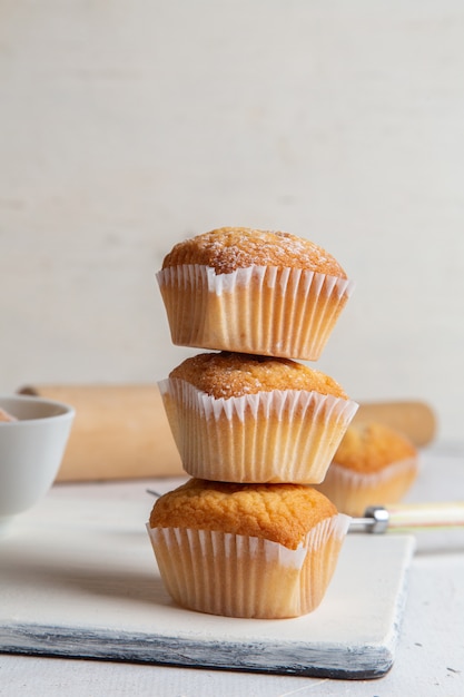 Vorderansicht von kleinen Kuchen innerhalb der Papierformen mit Zuckerpulver auf der weißen Oberfläche