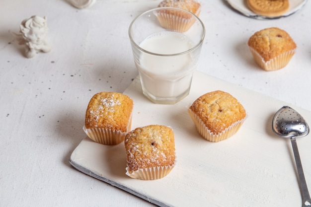 Vorderansicht von kleinen leckeren Kuchen mit Zuckerpulver und Glas Milch auf der weißen Oberfläche