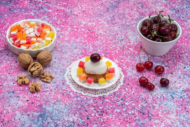 Vorderansicht von Kuchen und Kirschen zusammen mit Walnüssen und Marmeladen auf der farbigen Oberfläche