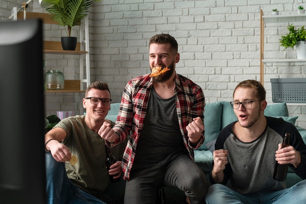 Vorderansicht von männlichen Freunden, die Sport im Fernsehen beobachten und Pizza haben