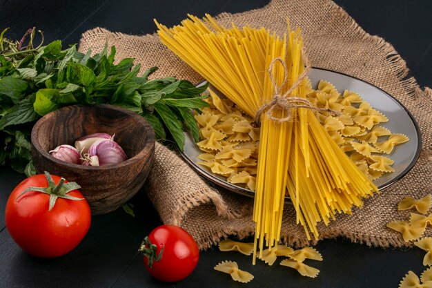 Vorderansicht von rohen Nudeln mit rohen Spaghetti auf einem Teller mit Tomaten Knoblauch und einem Bündel Minze auf einer beigen Serviette
