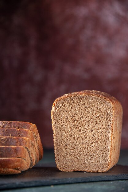 Vorderansicht von Schwarzbrotscheiben auf schwarzem Holztablett auf gemischtem, beunruhigtem Hintergrund