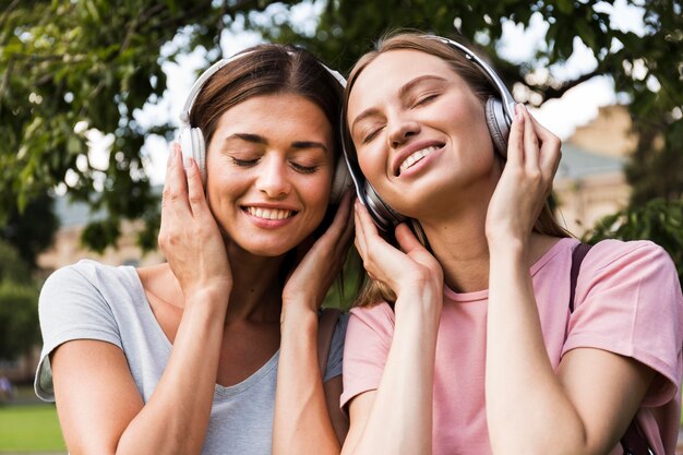 Vorderansicht von Smiley-Frauen im Freien, die Musik auf Kopfhörern hören