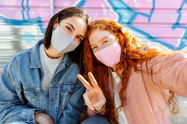 Vorderansicht von Smiley-Freundinnen mit Gesichtsmasken im Freien, die ein Selfie nehmen