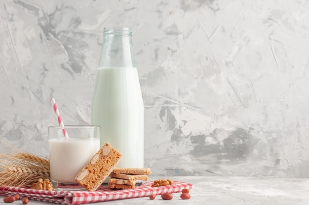 Vorderansicht von stabförmigen Süßigkeiten in Glasbecherflasche gefüllt mit Milch und Gebäck Erdnüsse auf rot gestreiftem Handtuch auf der rechten Seite auf grauem Hintergrund