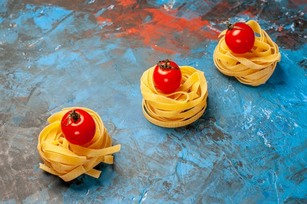 Vorderansicht von Tomaten auf hausgemachter Pasta, die in einer Reihe auf blauem Hintergrund aufgereiht sind