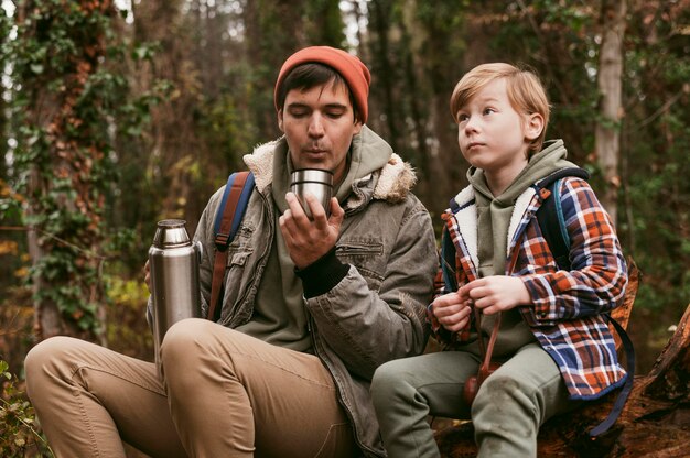 Vorderansicht von Vater und Sohn, die heißen Tee draußen in der Natur haben