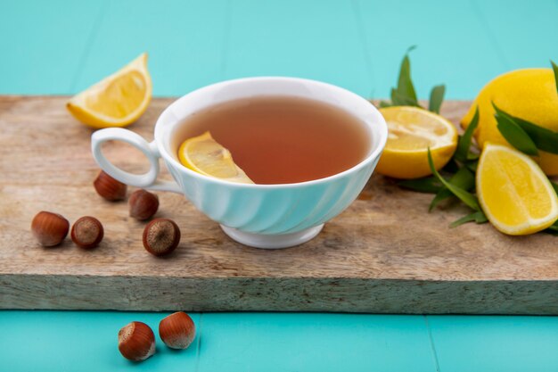 Vorderansicht von Zitronen auf einem hölzernen Küchenbrett mit einer Tasse Tee-Haselnüssen auf blauer Oberfläche