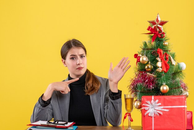 Vorderansicht wanderte Mädchen, das am Schreibtisch sitzt und Weihnachtsbaum und Geschenkcocktail zeigt