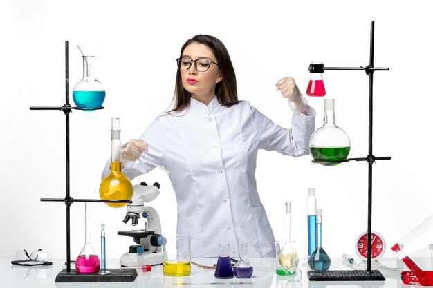 Vorderansicht weibliche Chemikerin im sterilen medizinischen Anzug, der um Tisch mit Lösungen auf der weißen Hintergrundviruskrankheit Covid Lab Pandemic Science steht
