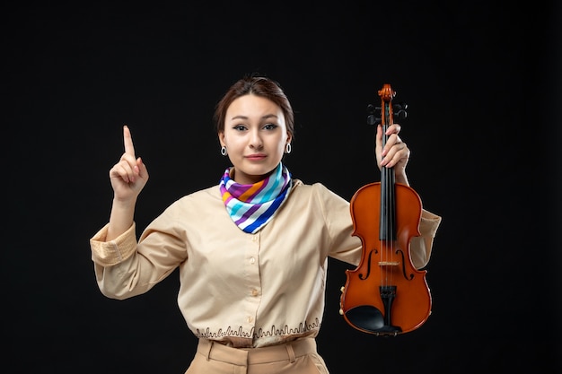 Vorderansicht weibliche Geigerin hält ihre Geige auf dunkler Wand Konzert Melodie spielen Instrument Frau Leistung Emotion