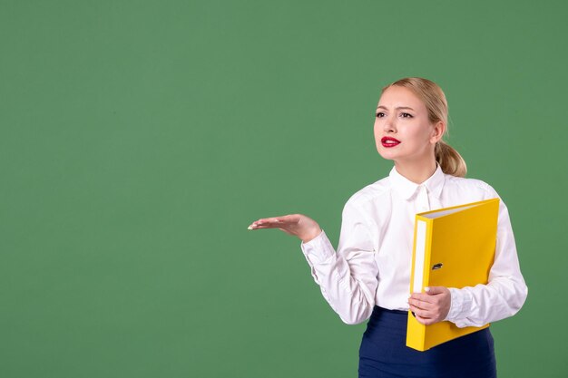 Vorderansicht weibliche Lehrerin im Gespräch mit jemandem auf grünem Hintergrund Unterrichtsbuch Studium Bibliotheksarbeit Universitätsuniform Schülerschule