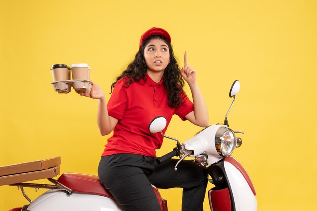 Vorderansicht weiblicher Kurier auf Fahrrad, der Kaffeetassen auf gelbem Hintergrund hält Arbeiterservice einheitliche Frauenlieferungsarbeit