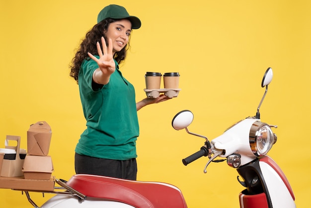 Vorderansicht weiblicher Kurier in grüner Uniform mit Kaffee auf gelbem Hintergrund Farbe Job Lieferung Arbeit Essen Frau Service Arbeiter