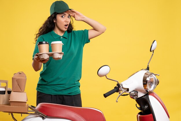 Vorderansicht weiblicher Kurier in grüner Uniform mit Kaffee auf gelbem Hintergrund Service Arbeiter Job Lieferung Arbeit Essen Frau Farbe