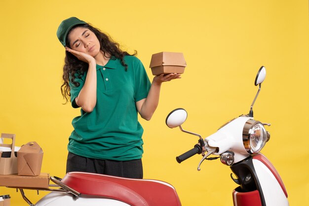 Vorderansicht weiblicher Kurier in grüner Uniform mit kleinem Lebensmittelpaket auf gelbem Hintergrund Arbeitsfarben Job Delivery Food Woman Service Worker