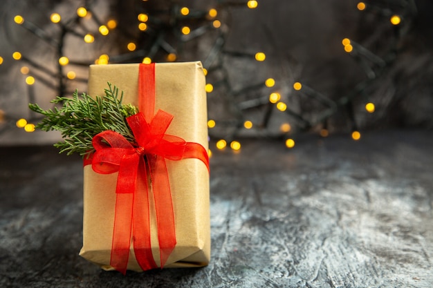 Kostenloses Foto vorderansicht weihnachtsgeschenk mit rotem band auf dunklem hintergrund weihnachtslichter gebunden