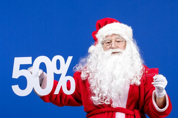 Vorderansicht weihnachtsmann, der bankkarte hält und auf blauem urlaubsgeschenk weihnachten schreibt