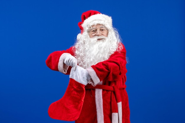 Kostenloses Foto vorderansicht weihnachtsmann, der große weihnachtssocke auf dem blauen weihnachtsschnee hält