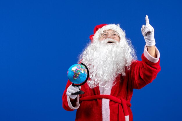 Vorderansicht weihnachtsmann, der kleine erdkugel auf blauem weihnachtsfeiertag neues jahr hält