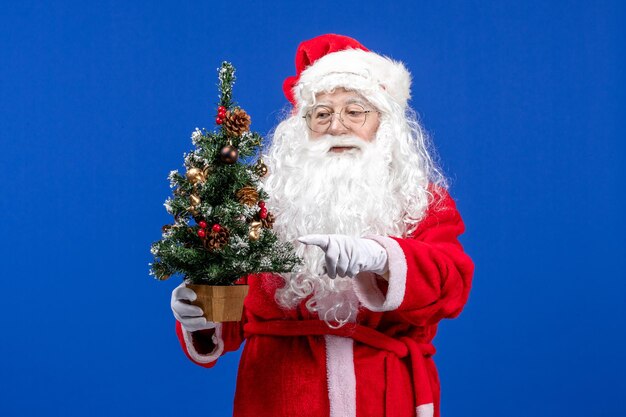Vorderansicht weihnachtsmann, der kleinen neujahrsbaum auf der blauen schneefarbe weihnachten neues jahr hält