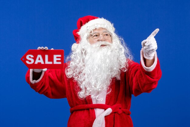 Vorderansicht weihnachtsmann, der rote verkaufsschrift auf blauem bodenfarbe schneeurlaub neues jahr weihnachten hält
