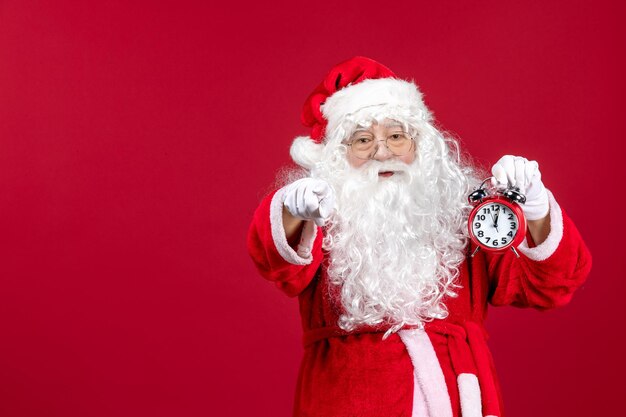 Vorderansicht weihnachtsmann, der uhr auf rotem weihnachtsemotionsurlaub neues jahr hält