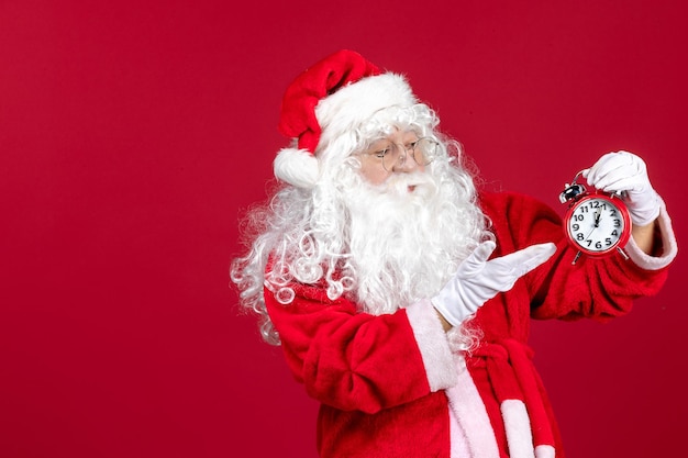 Vorderansicht weihnachtsmann, der uhr auf rotem weihnachtsfeiertag neues jahr emotionale zeit hält