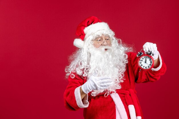 Vorderansicht weihnachtsmann hält uhr an roten weihnachtsfeiertagen neues jahr emotion