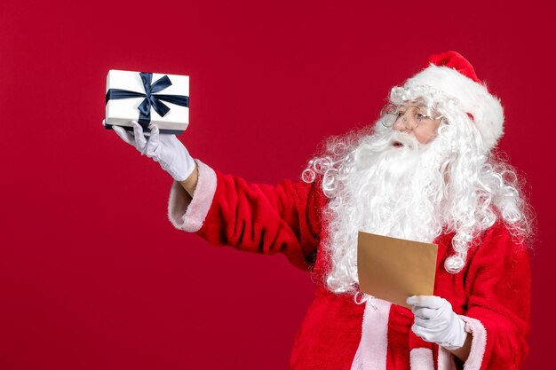 Vorderansicht Weihnachtsmann liest Brief vom Kind und hält Geschenk auf rotem Emotionen Geschenk Weihnachtsfeiertag