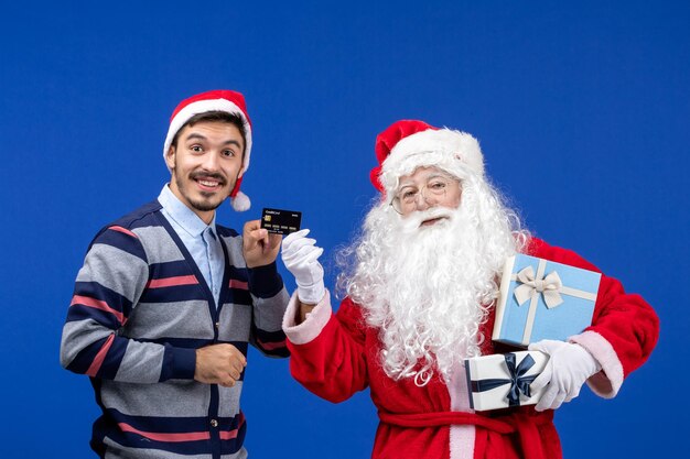 Vorderansicht weihnachtsmann mit geschenken und jungem mann, der bankkarte auf blauem weihnachtsgefühl hält