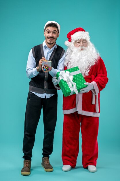 Vorderansicht Weihnachtsmann mit jungem Mann, der Notizen auf dem blauen Hintergrund macht