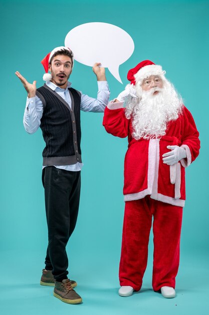 Vorderansicht-Weihnachtsmann mit jungem Mann, der weißes Zeichen auf dem blauen Hintergrund hält