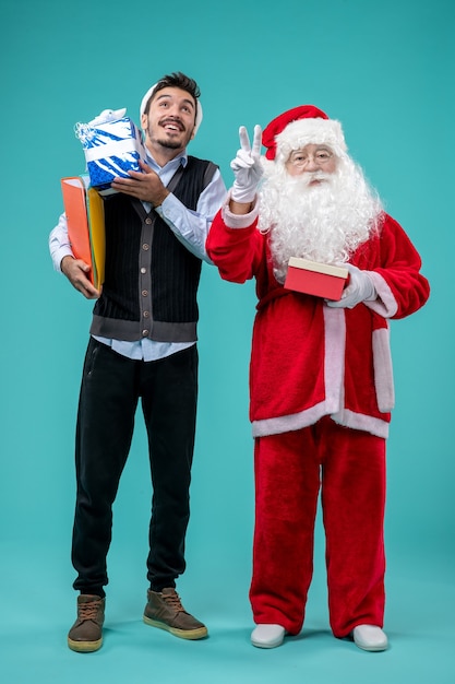 Vorderansicht Weihnachtsmann mit jungem Mann und Geschenken auf blauem Schreibtisch