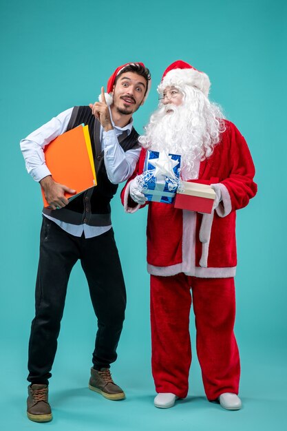 Vorderansicht Weihnachtsmann mit jungem Mann und Geschenken auf blauem Schreibtisch