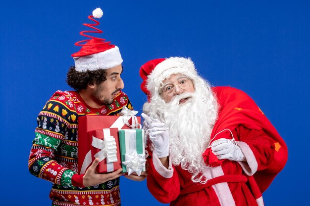 Vorderansicht weihnachtsmann mit jungem mann und verschiedenen geschenken auf blauer emotionen weihnachtsfeiertagsfarbe