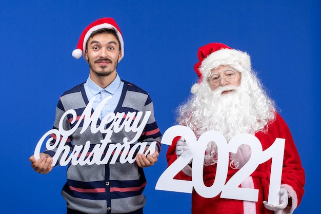 Vorderansicht weihnachtsmann mit jungen männlichen halten und frohen weihnachten schriften auf blauem weihnachtsfeiertag