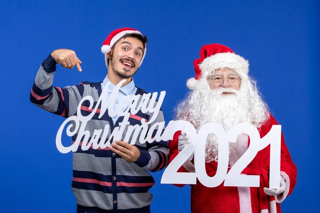 Vorderansicht weihnachtsmann mit jungen männlichen halten und frohen weihnachten schriften auf blauem weihnachtsfeiertag